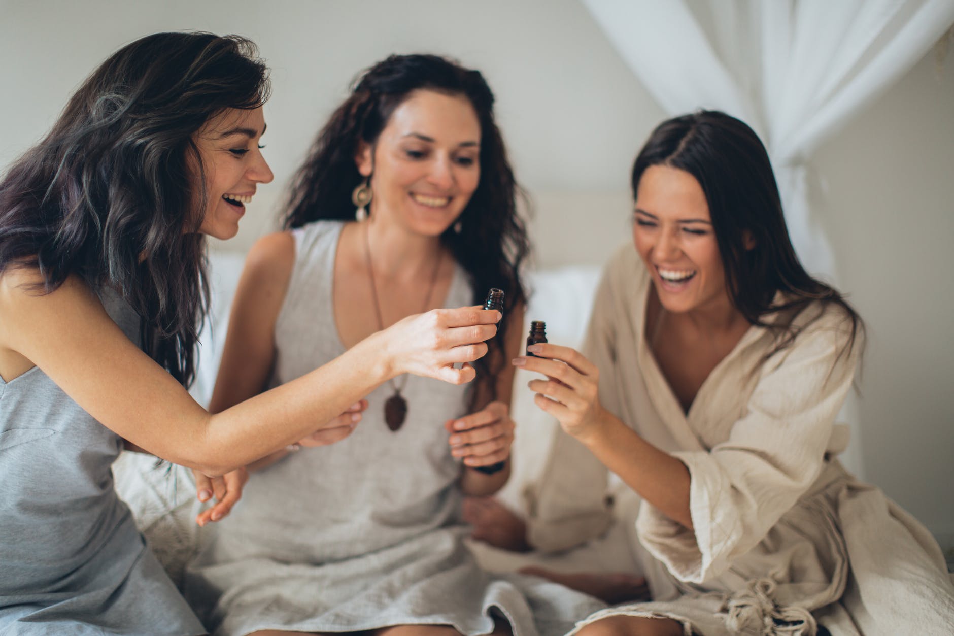 women sitting on the bed laughing while holding a glass bottles